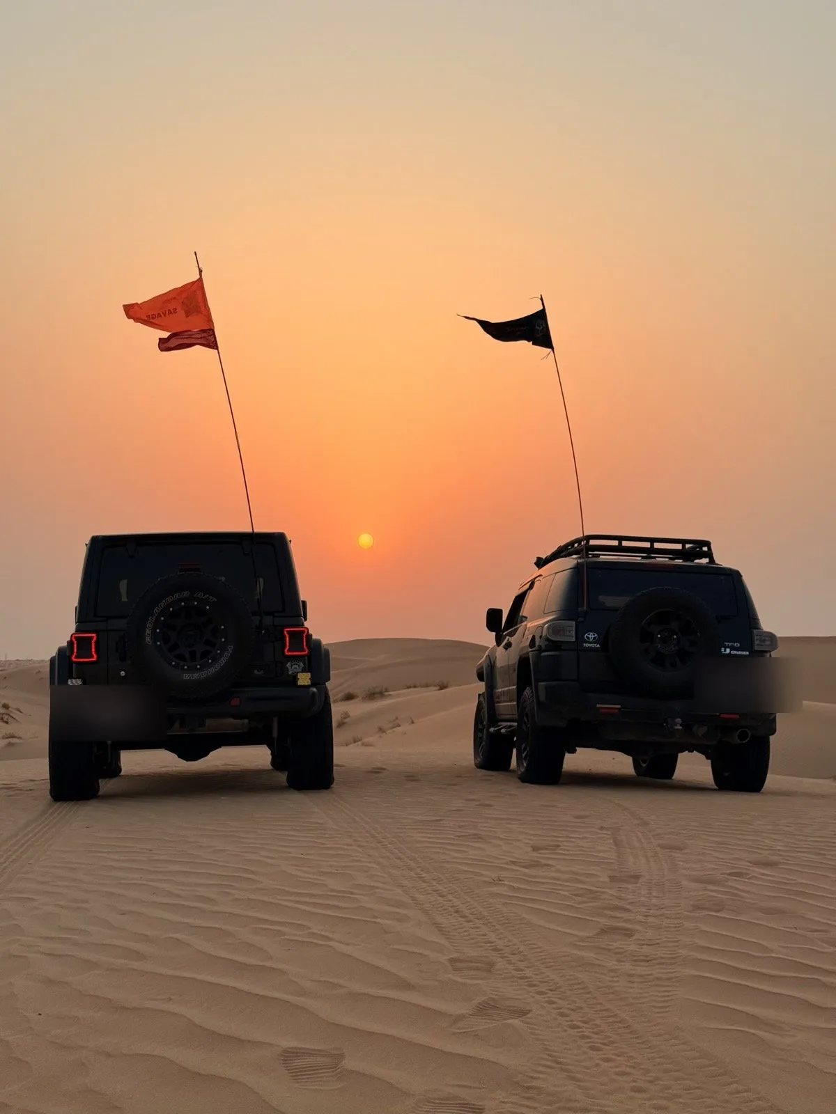 Two flagged 4x4s facing the sunset over the Al Faya sands
