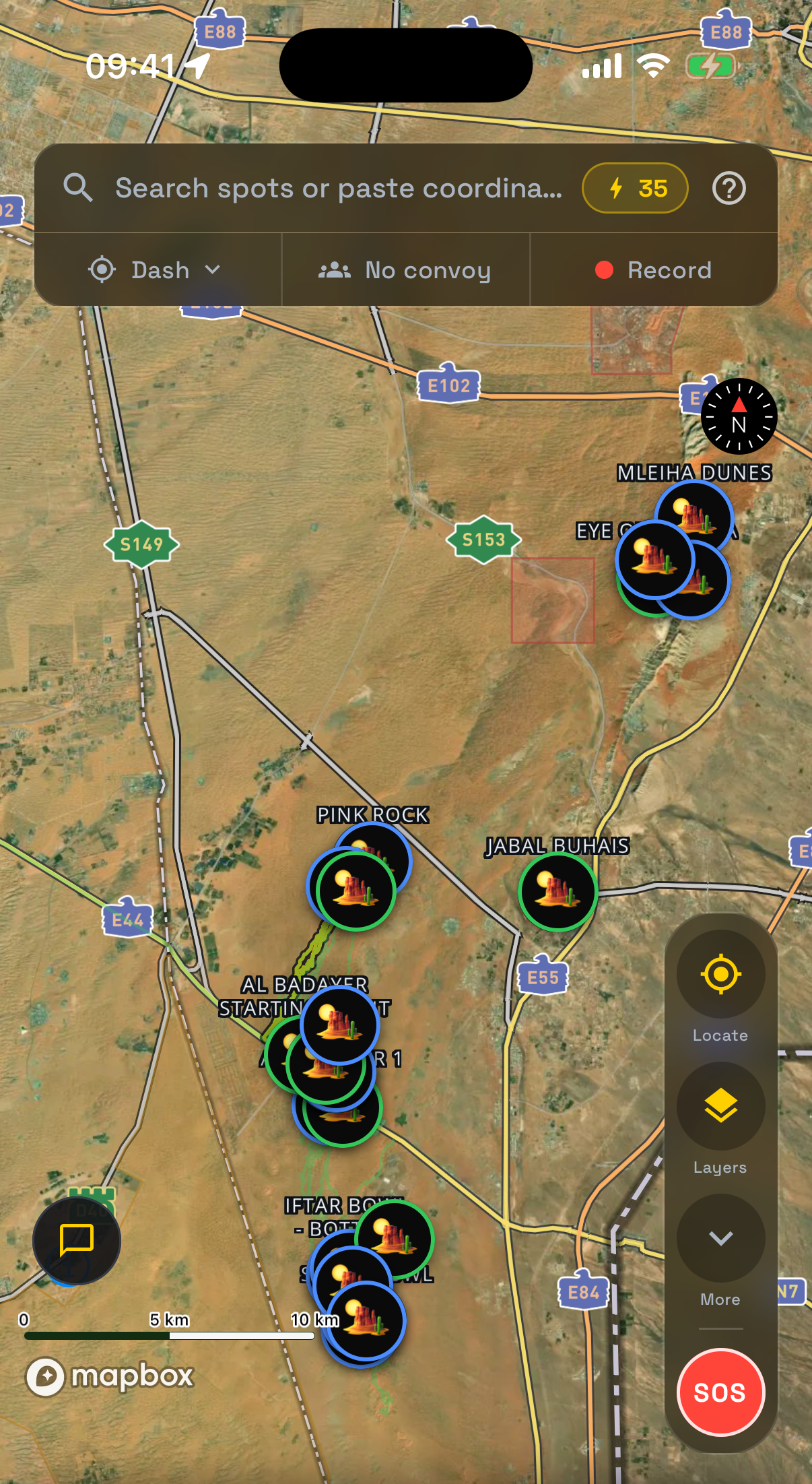 The Live Map in the app: a satellite view of the desert east of Dubai with named off-road spots, the search bar, and an SOS button on the side rail