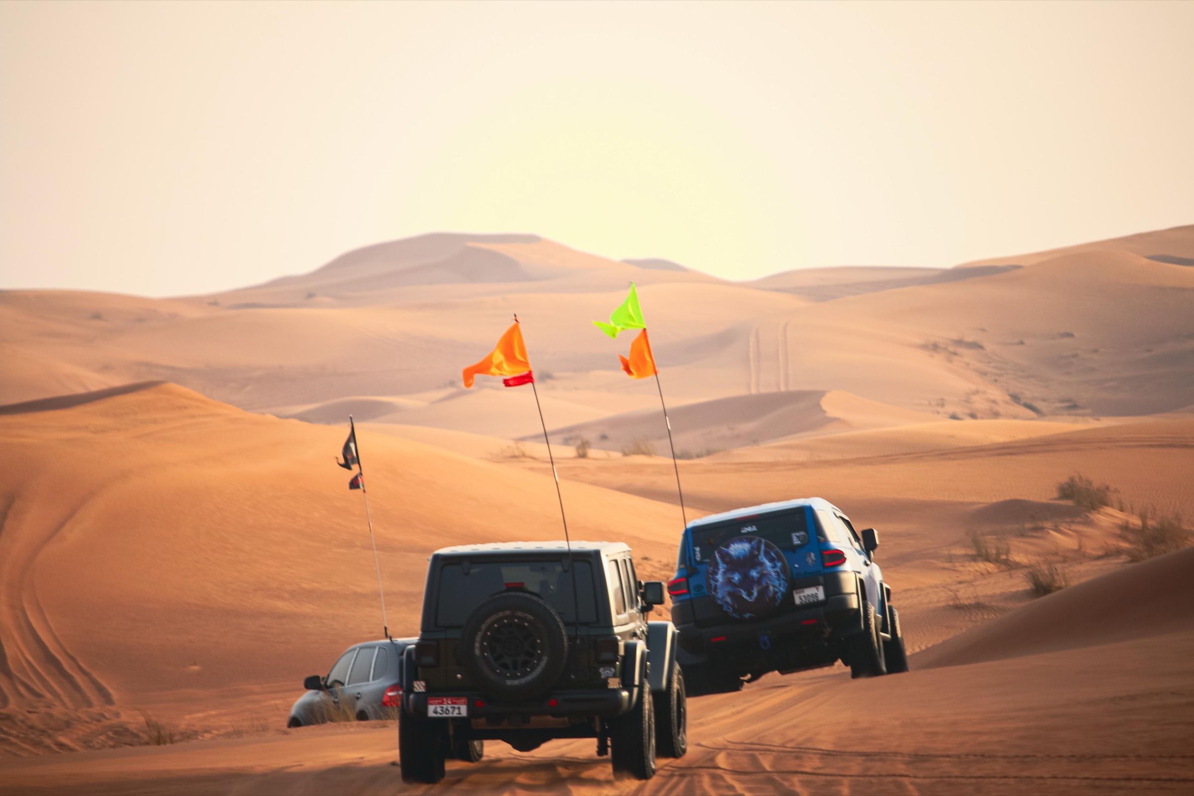A convoy of three 4x4s with dune flags crossing golden dunes in the UAE at sunset