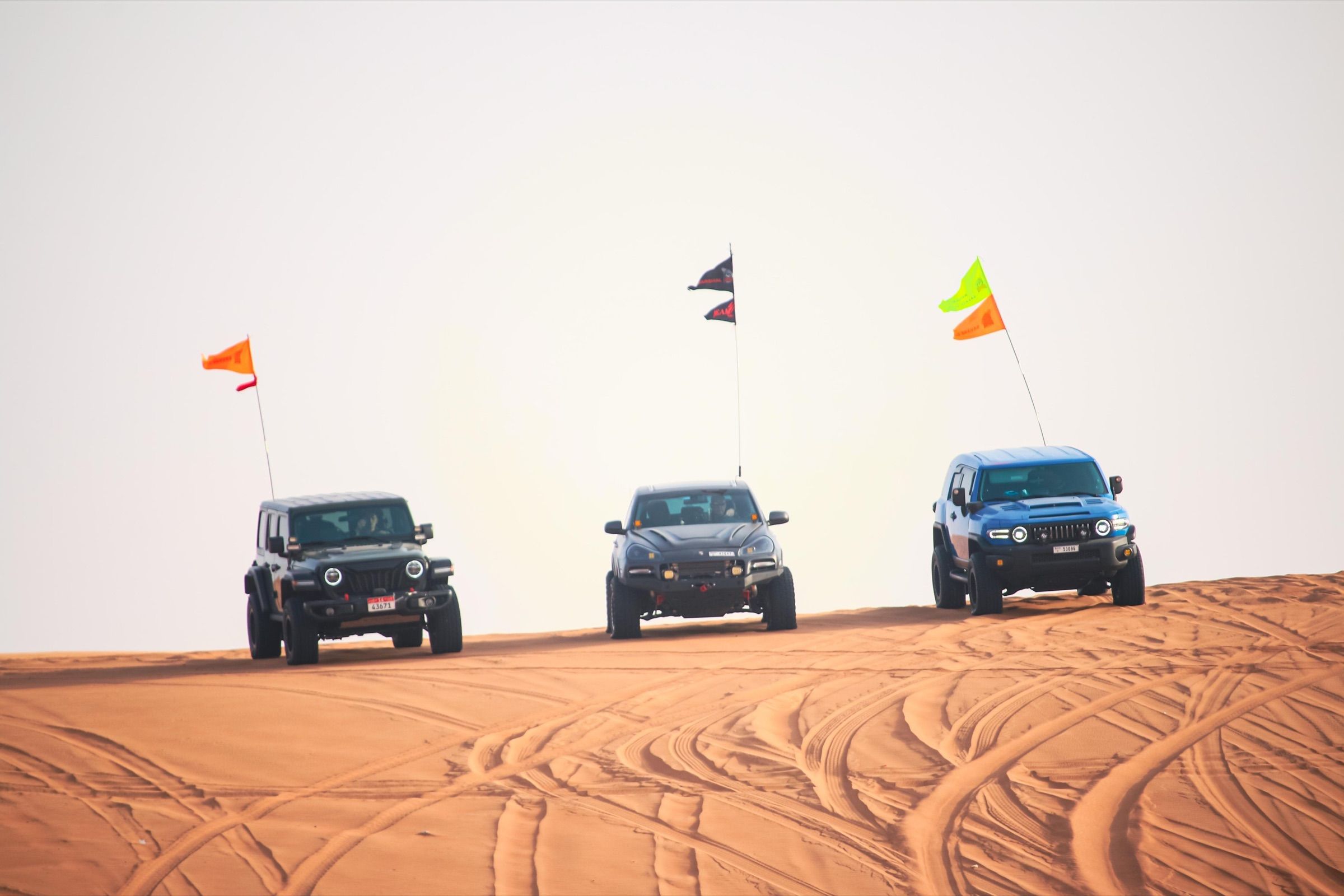 Three 4x4s with dune flags lined up on a dune crest in the UAE desert