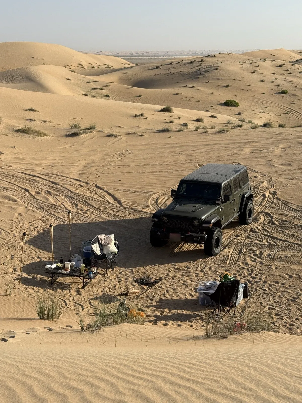 A desert camp beside a 4x4 — chairs, table and gear laid out on the sand
