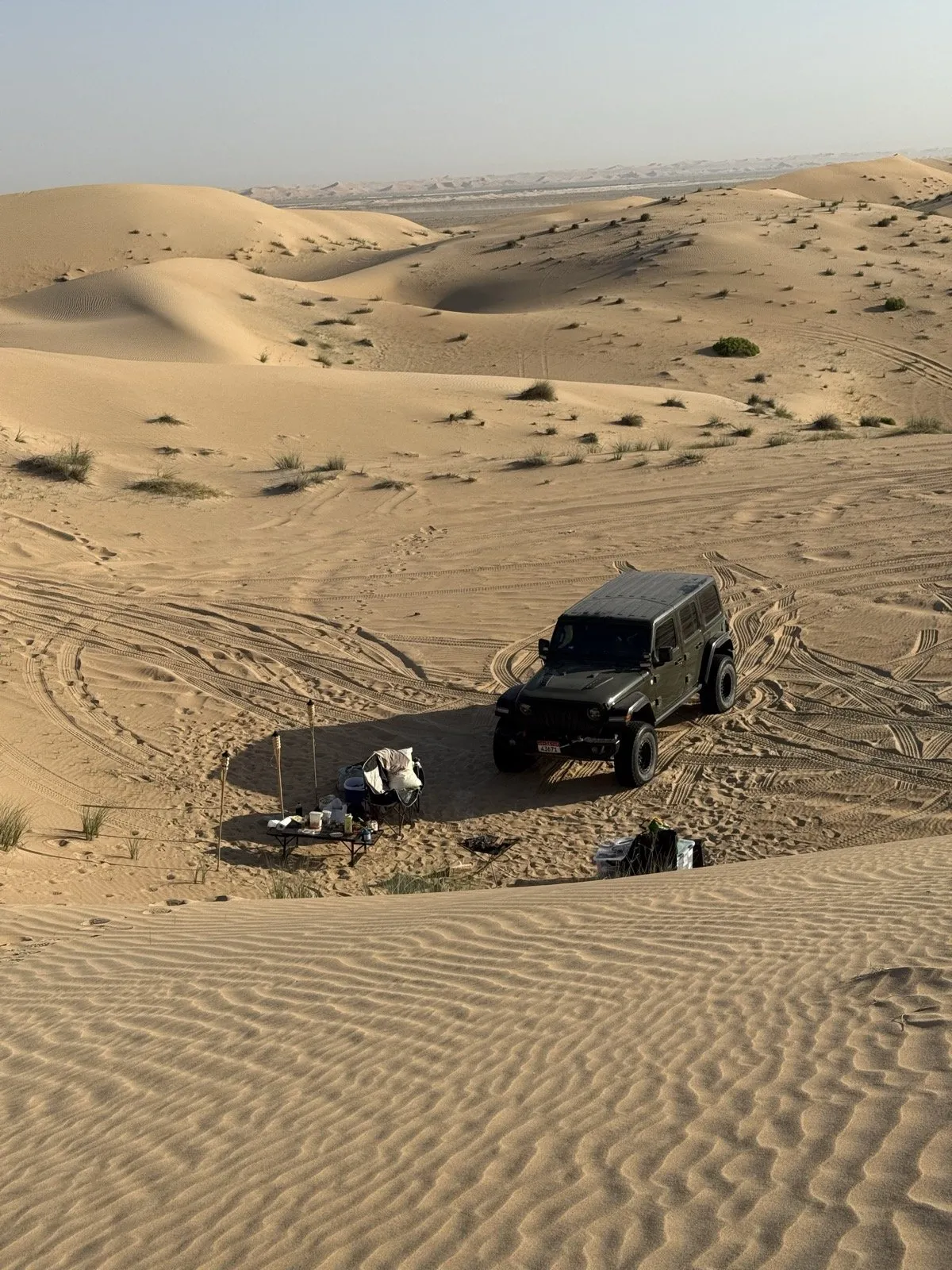 A morning desert camp beside a 4x4 on the Sweihan sand — chairs, table and gear on the sand