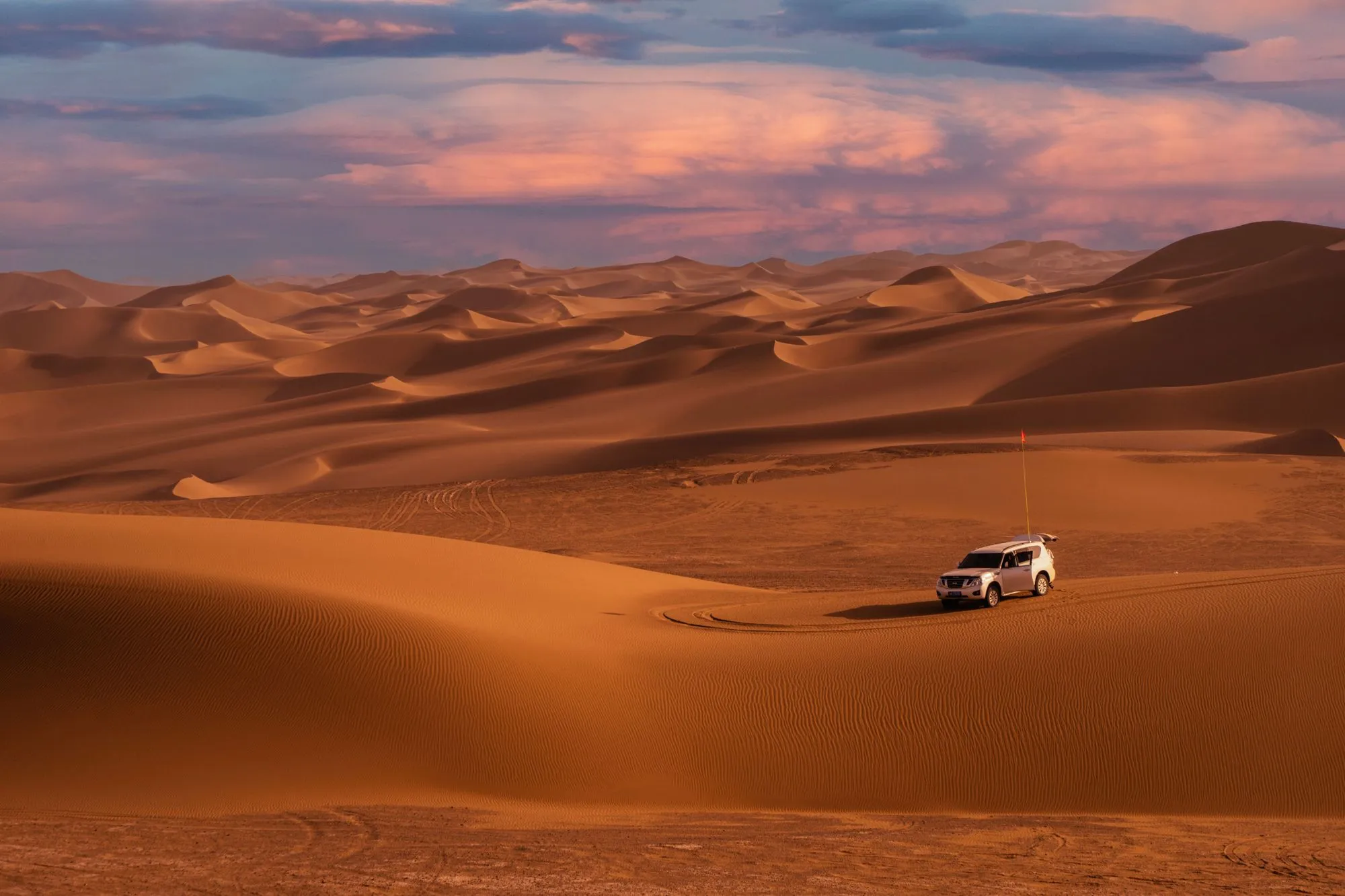A single 4x4 with a dune flag parked alone in a large dune field at dusk