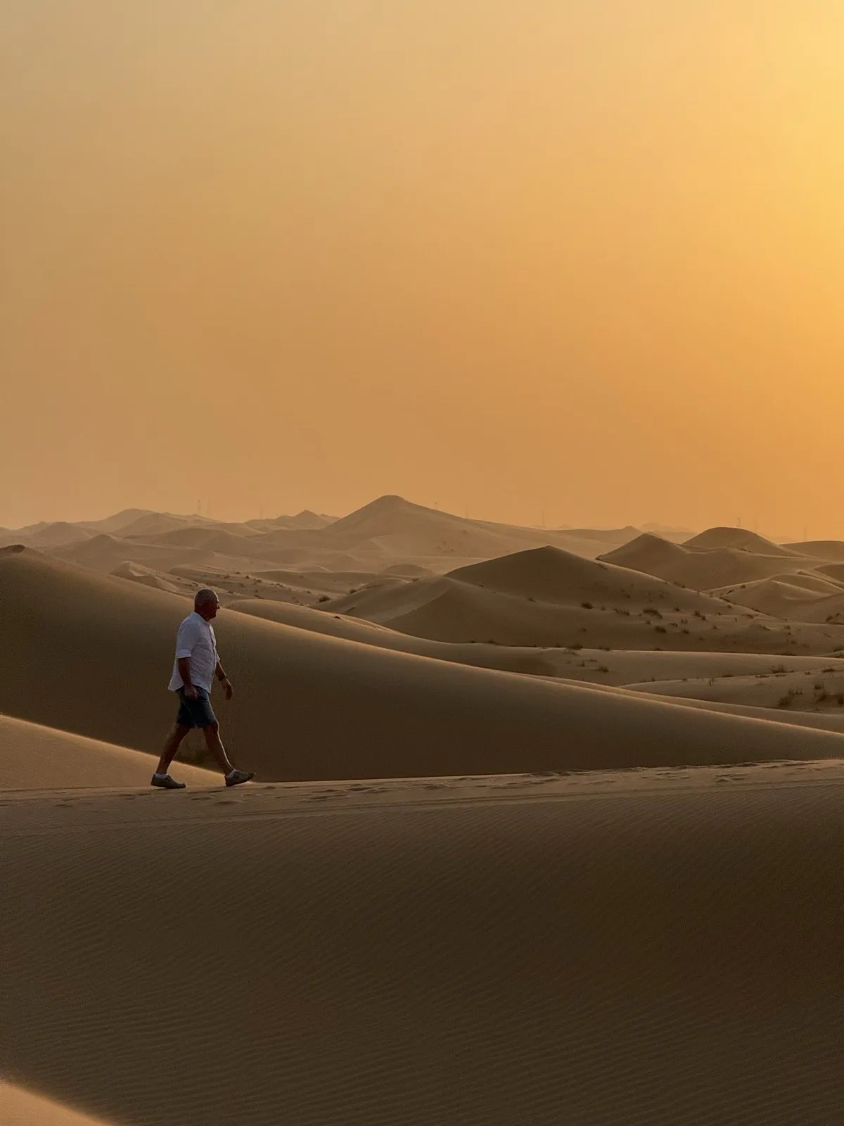 A driver walking a dune ridge at sunset to read the ground ahead