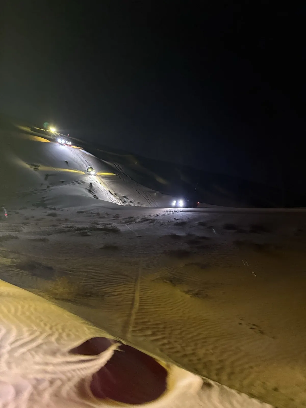 A convoy's headlights working up a dune line after dark in the Liwa desert