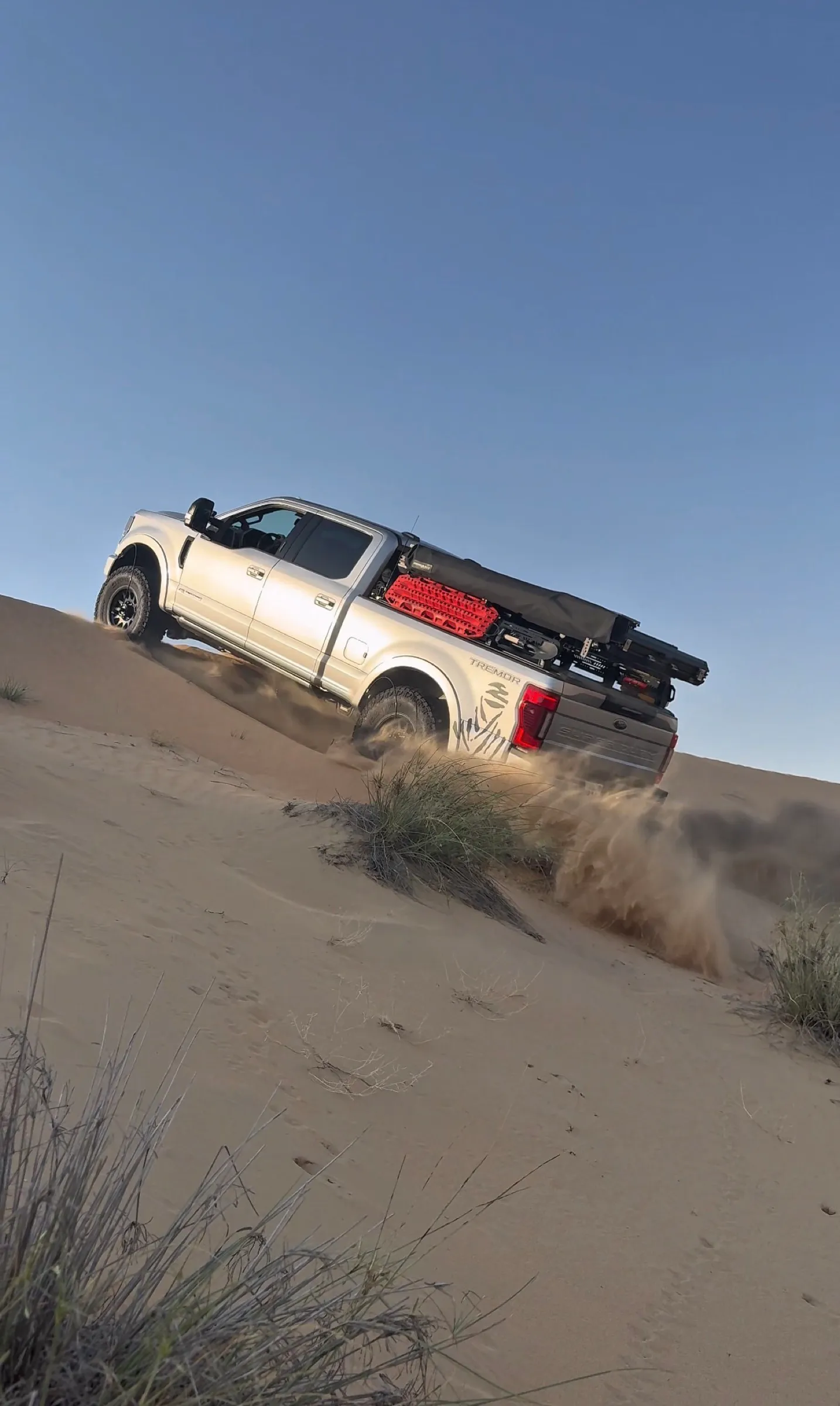 A pickup carrying recovery boards climbing a dune in golden light