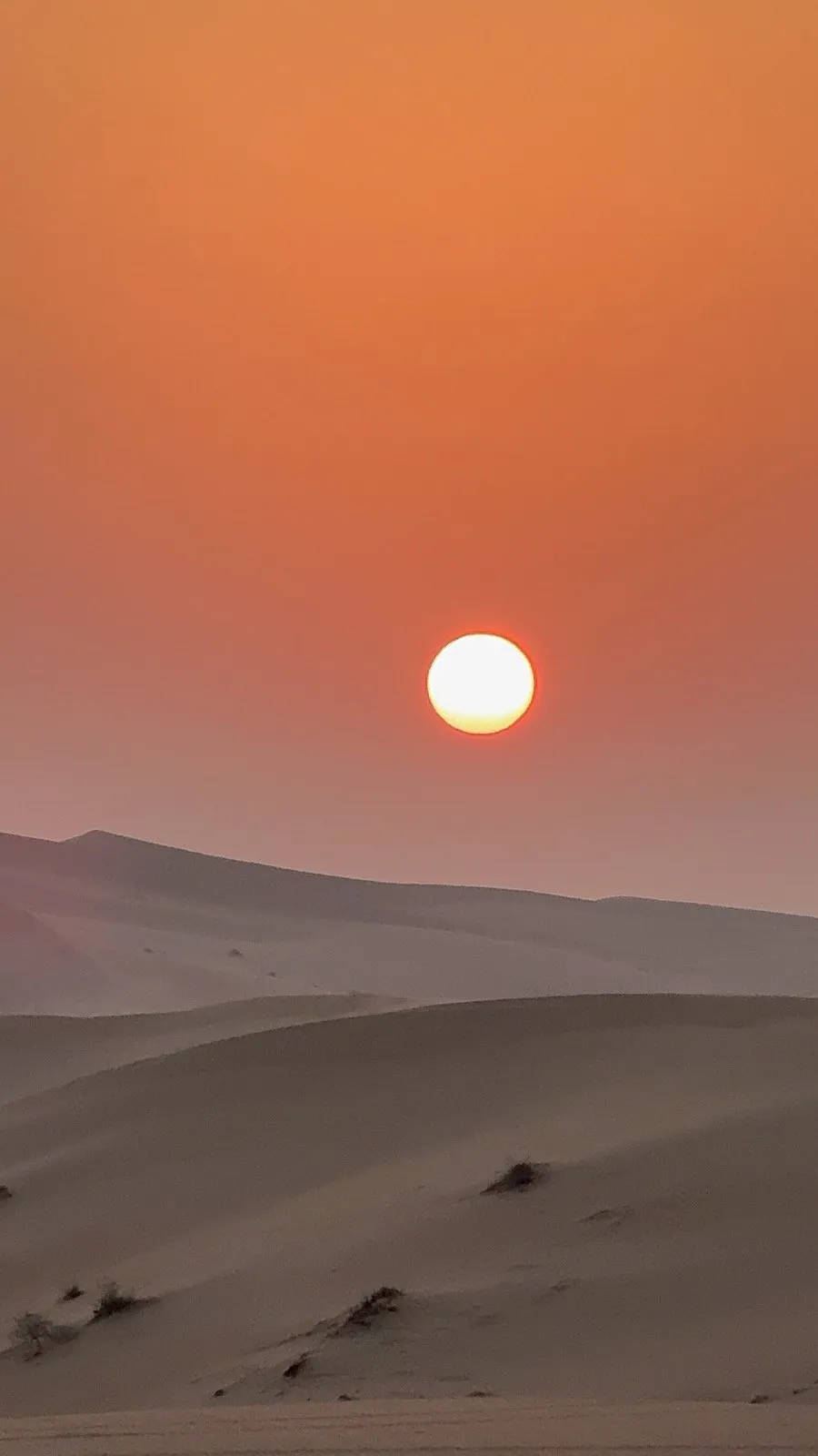 A red sun barely visible through thick dust haze over the dunes