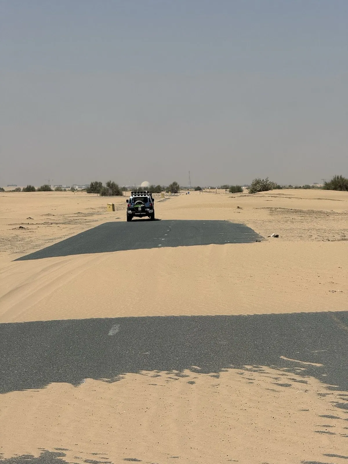 Wind-blown sand crossing a paved desert road, half burying the lane