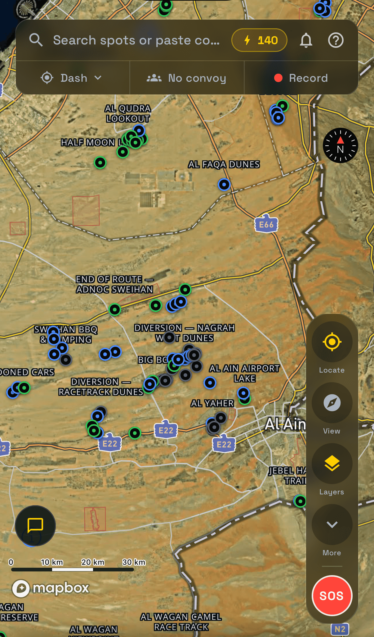 The OffroadPal live map: a satellite view of the dunes around Al Ain with spot pins ringed by grade, the search bar that also takes pasted coordinates, the notification bell, and the Locate, View, Layers and SOS buttons