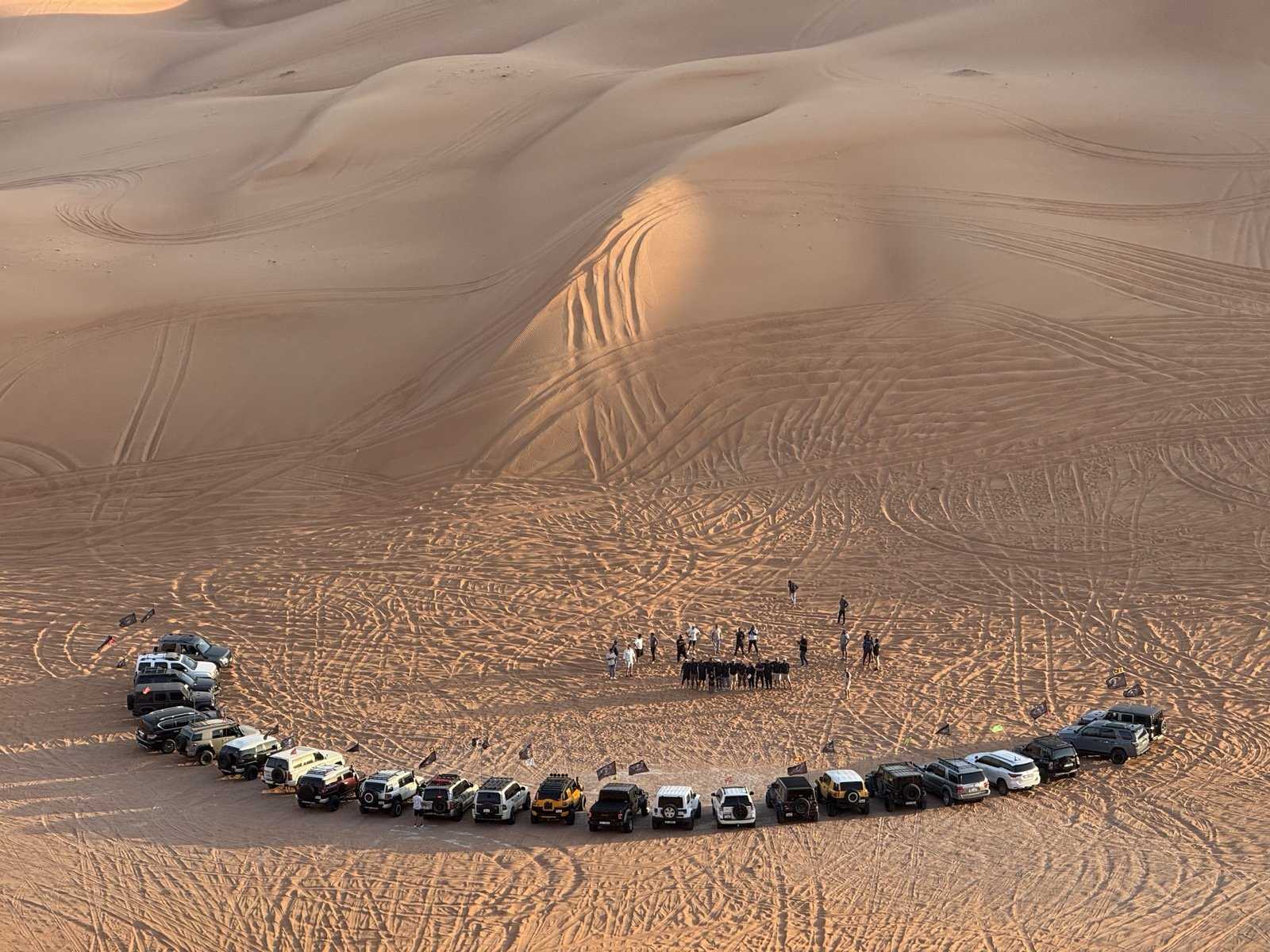 A ring of 4x4s parked in a wide dune bowl in the UAE